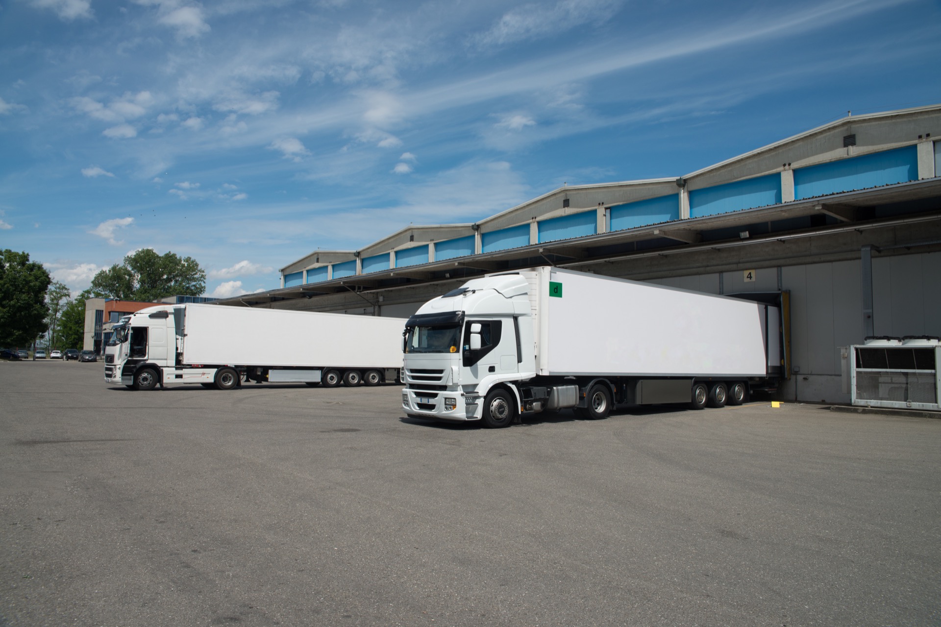 Semi-trailer trucks parked at the loading docks of a logistics warehouse under a blue sky.